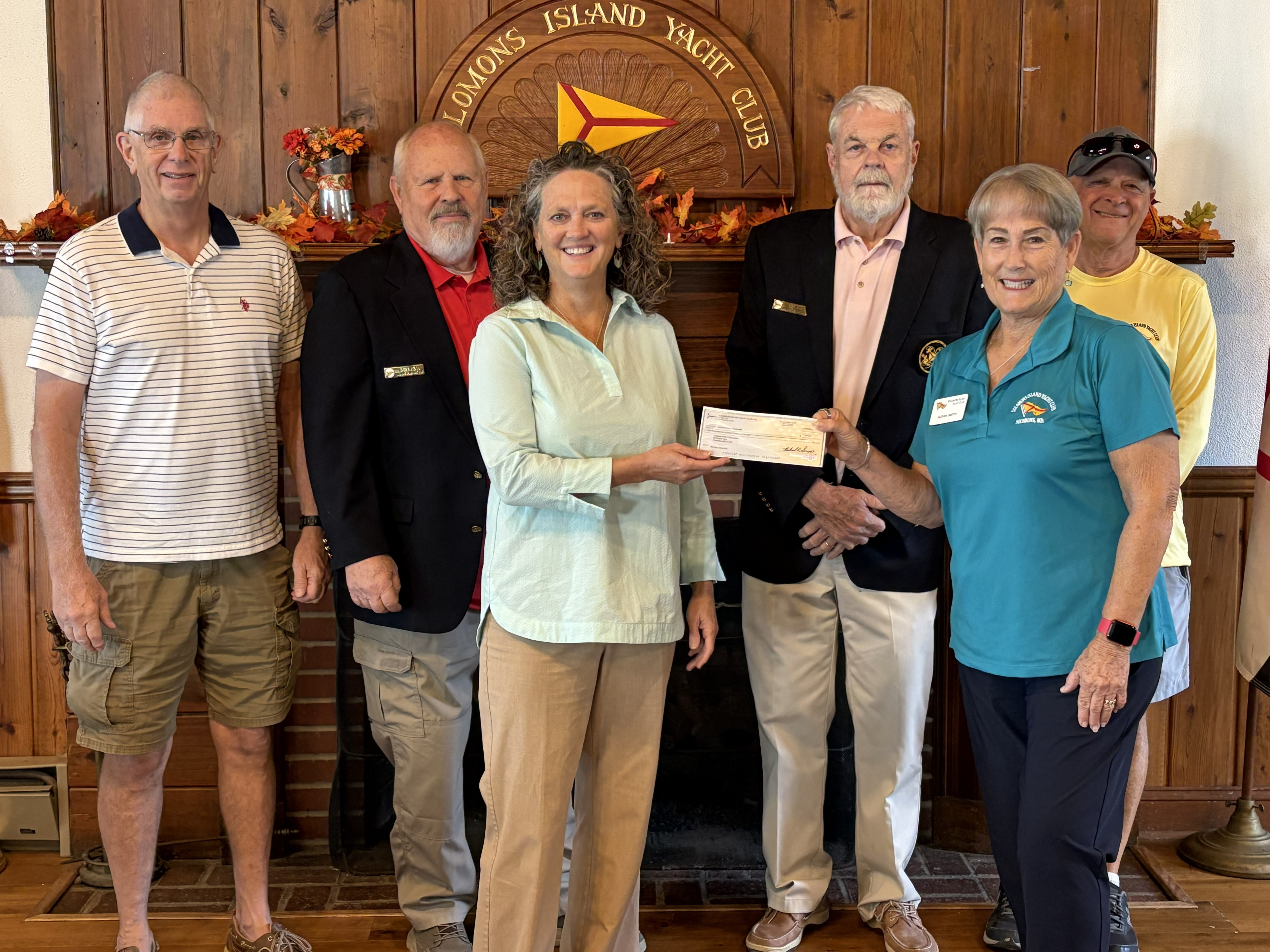 Four men and two women stand together holding a charity fundraising check