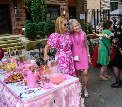 Two women in pink dresses pose for picture next to pink table