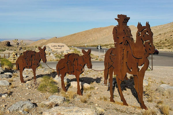 Sheet metal cutout sculpture of a cowboy on a horse leading two pack mules.