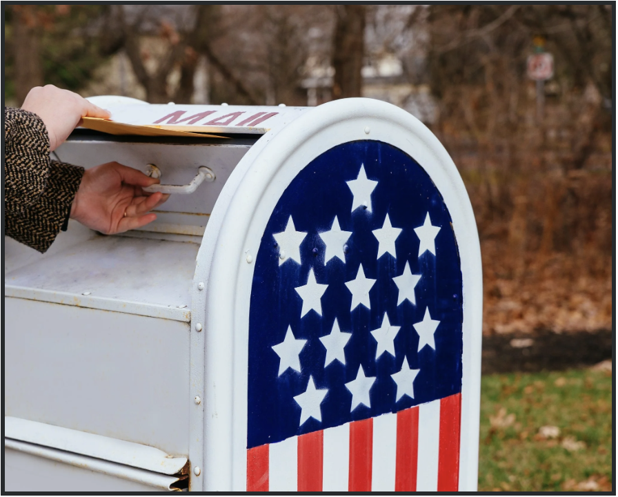 Hand on mailbox with stars and stripes in front of home