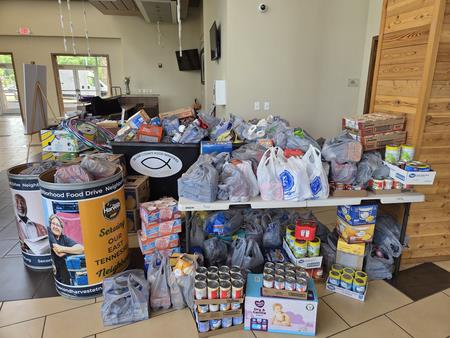 Table filled with assorted donated food items, including canned goods, boxes, and bags, arranged for a charity collection