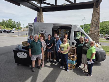 A van loaded with various donated items, including boxes and bags, with volunteers standing in front of van