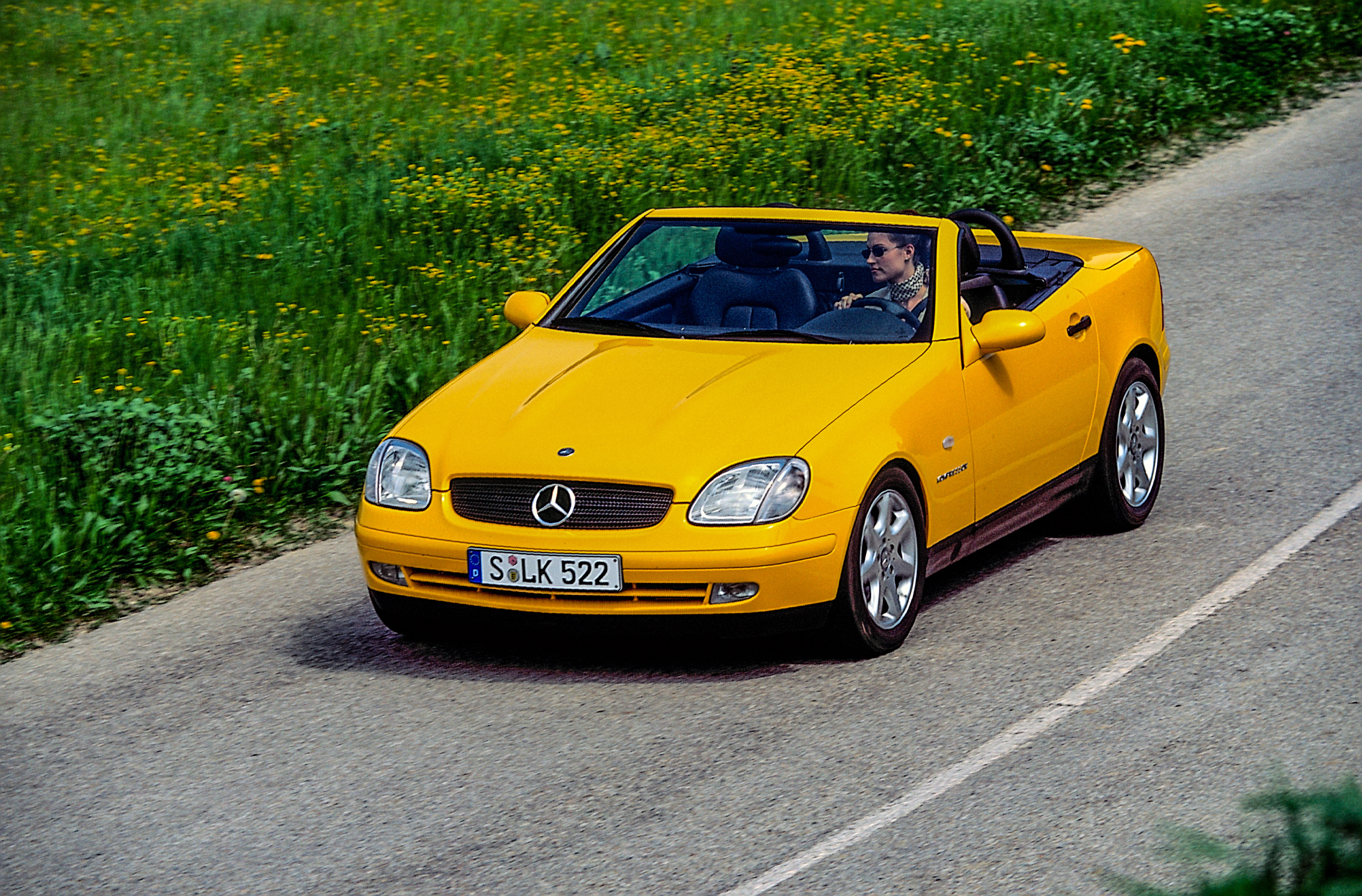 Mercedes-Benz SLK 230 Kompressor R 170 painted in yellowstone (Mercedes-Benz colour code 685). Driving shot with open soft top, from left front, from the year 1996.