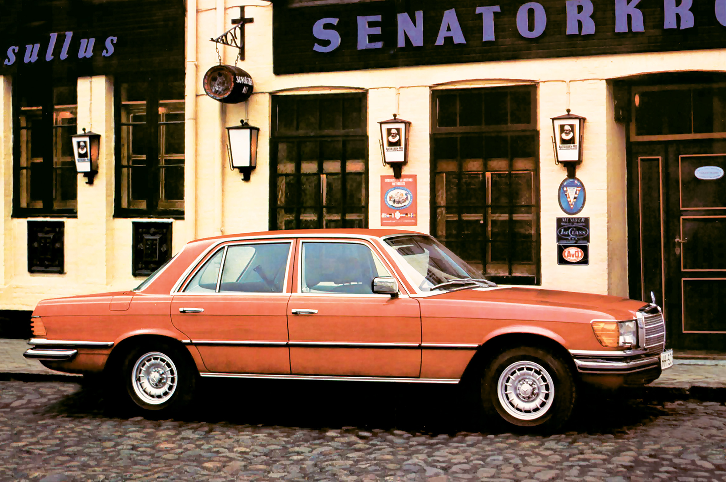 Orange Mercedes-Benz W116 parked in front of a restaurant.