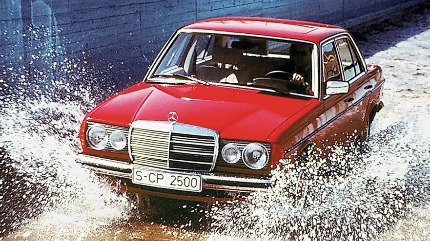 Red W123 driving through a puddle of water, splashing water up on either side