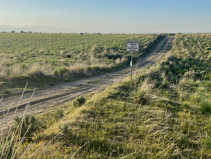 Dirt and gravel road with 'Primitive road no warning signs' sign