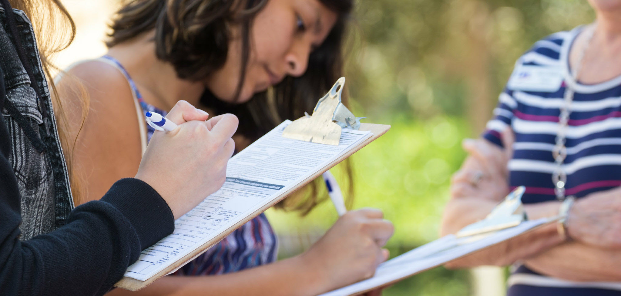 Young women holding clipboard, filling out a voter registration form.  Two other women are assisting
